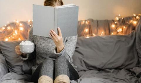 person reading a book and holding a cup of hot cocoa with fairy lights behind them