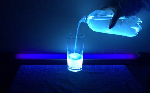 a hand holding a two liter bottle and pouring liquid into a glass. the liquid glows under blacklight