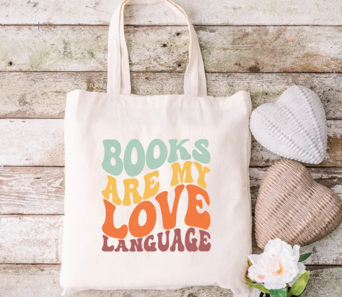 Off-white canvas tote bag with vinyl press that reads "Books are my love language" in colorful print. 