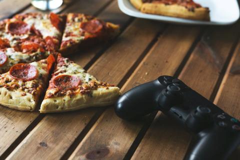 Pepperoni pizza slices on a wooden table next to a video game controller.