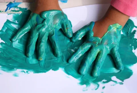 Child's hands covered in green paint pressing onto paper 