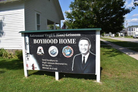 Sign outside the Virgil I. "Gus" Grissom Boyhood Home and Memorial featuring a photograph of the astronaut, an image of a Mercury Redstone rocket, and mission patches.