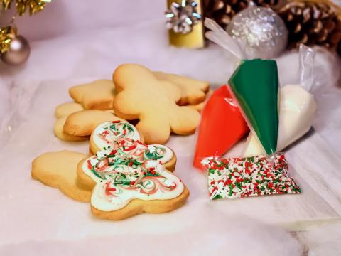 Christmas cookies in festive shapes are ready to decorate, surrounded by red, green, and white icing bags and colorful holiday sprinkles. 