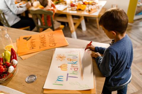 a young boy creates a colorful "I'm Thankful" poster at a table decorated with Thanksgiving crafts and autumn colors. 
