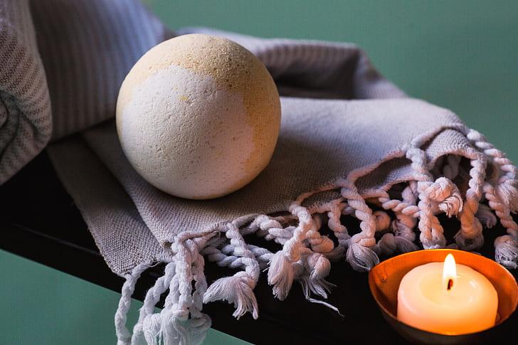 bath bomb sitting on  a towel with a small candle lit next to it