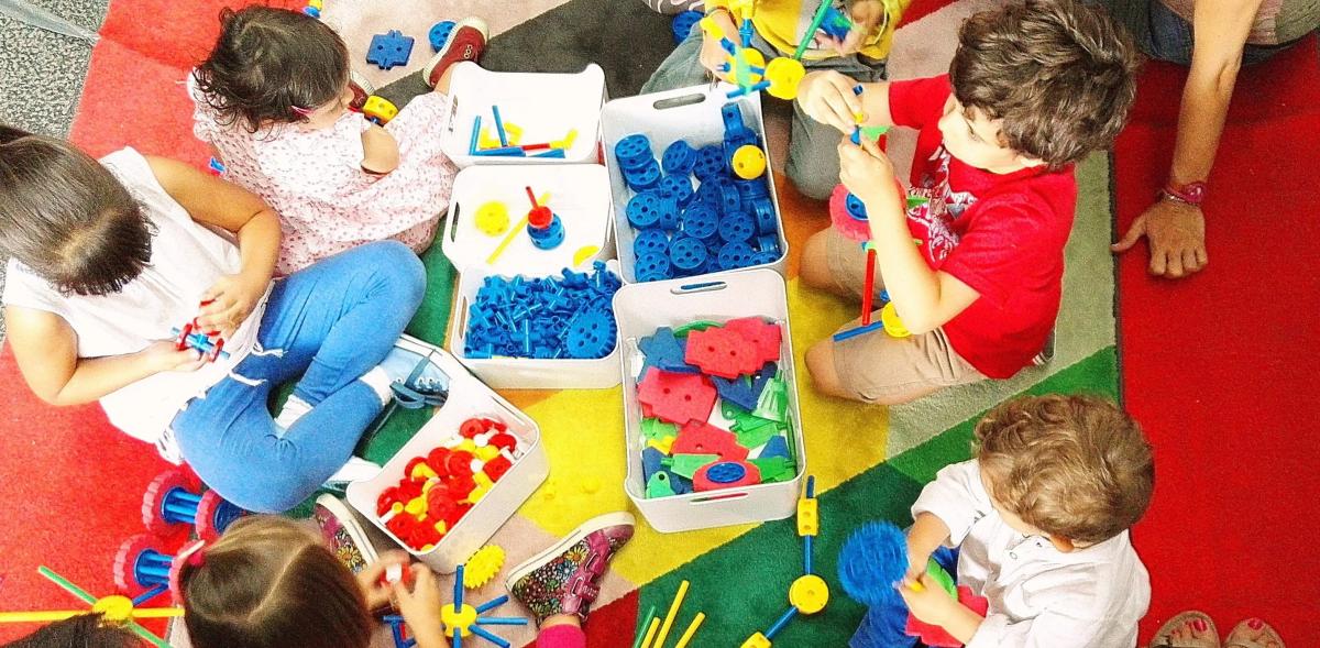 Children sitting on a colorful rug building with plastic construction toys.